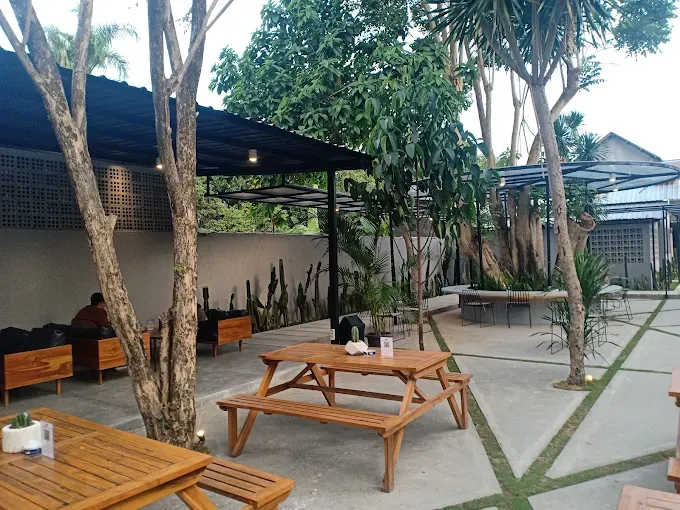 Area outdoor Kaktus Coffee Place dengan suasana tropis dan tanaman hijau.